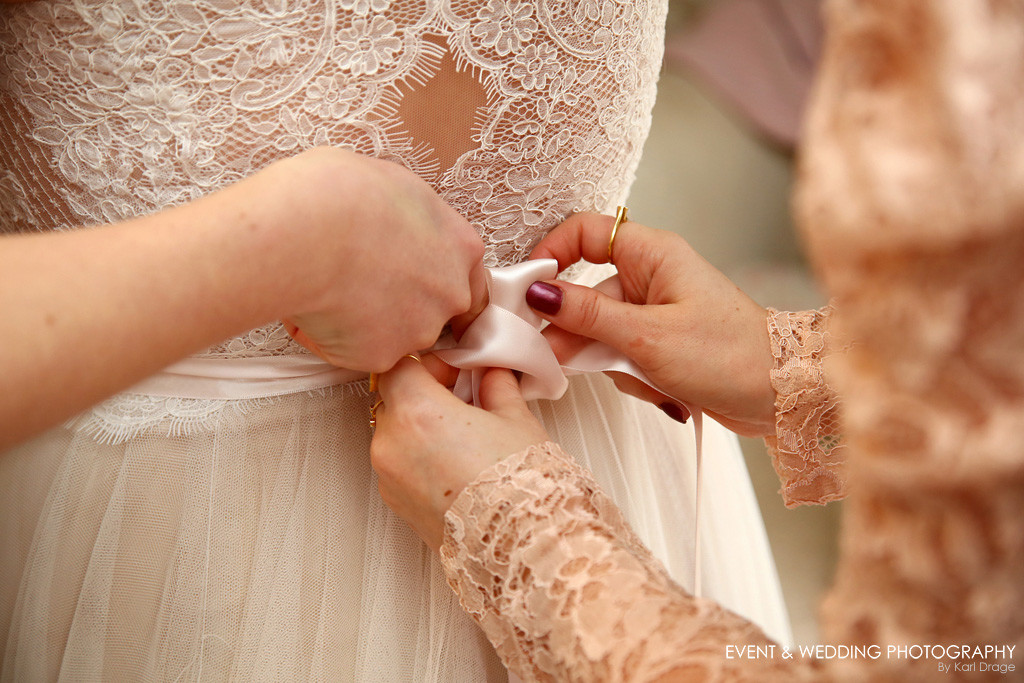 The bridesmaids tie the bow on the bride's dress.