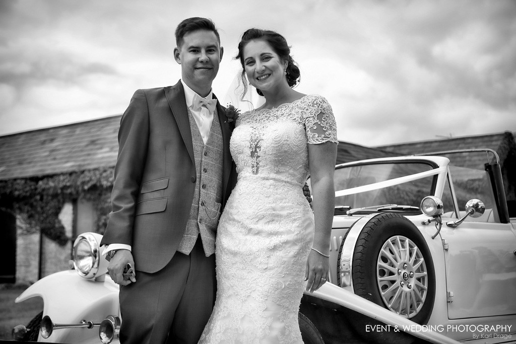 The bride and groom pose with their Beauford wedding car at their Huntsmill Farm wedding