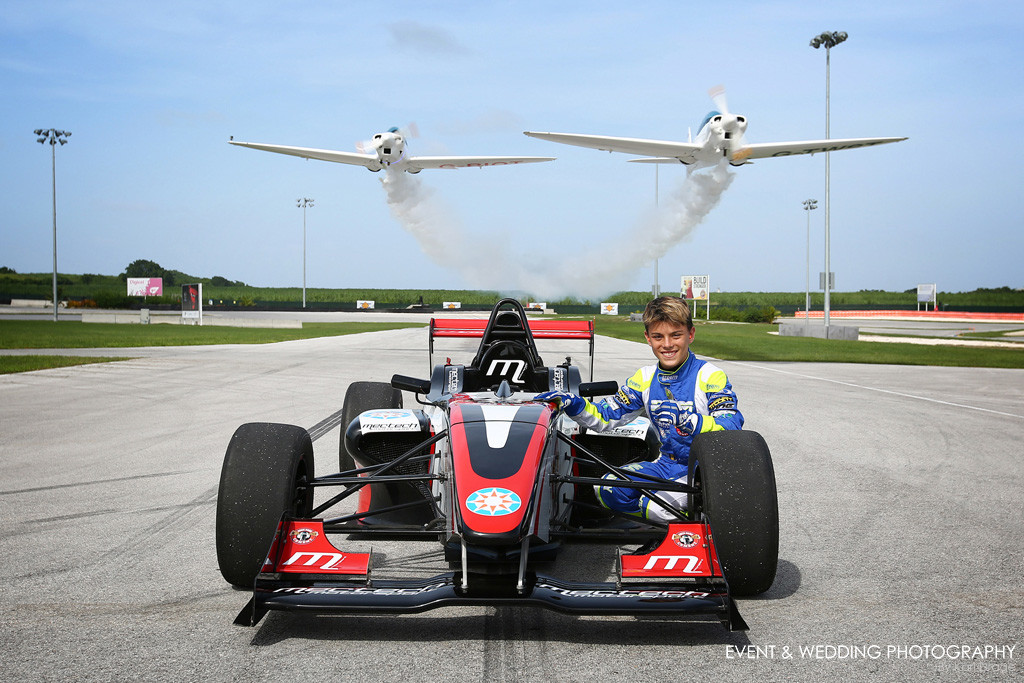 Zane Maloney poses with the Formula 4 car he would race against Jenson Button as the two Twister aeroplanes fly low overhead.