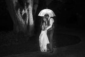 Bride and groom kissing in the dark under an umbrella on their very wet wedding day.