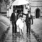 Bride and groom walking away from church under an umbrella