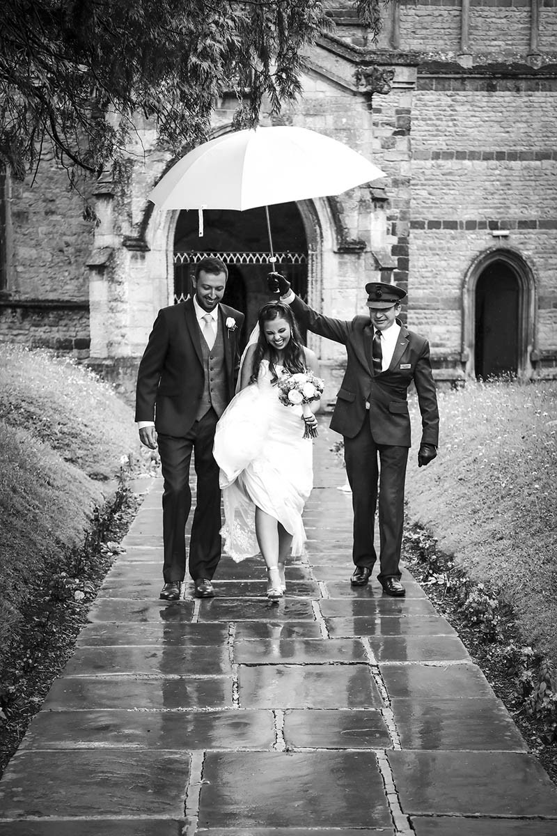 Bride and groom walking away from church under an umbrella