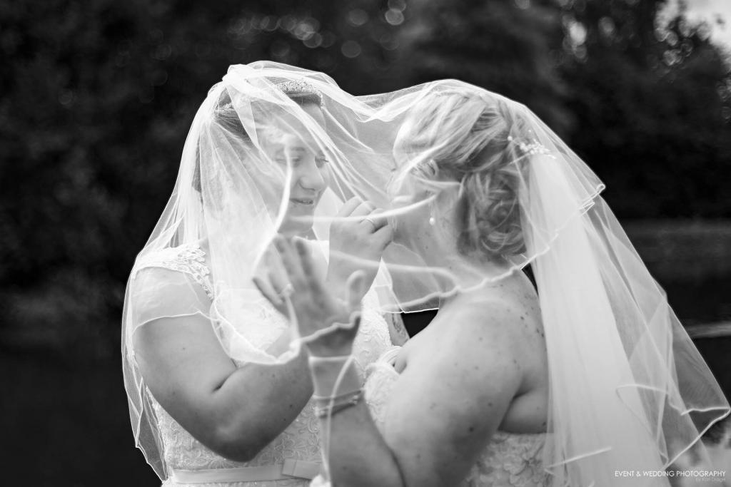 Black and white picture of two brides sharing a tender moment under their veils on their wedding day