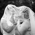 Black and white picture of two brides sharing a tender moment under their veils on their wedding day