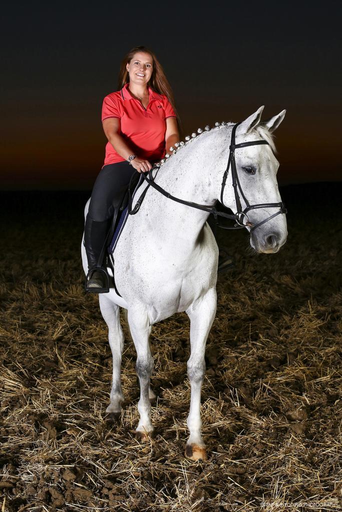 Horse and rider illuminated by studio lights in a field after dark