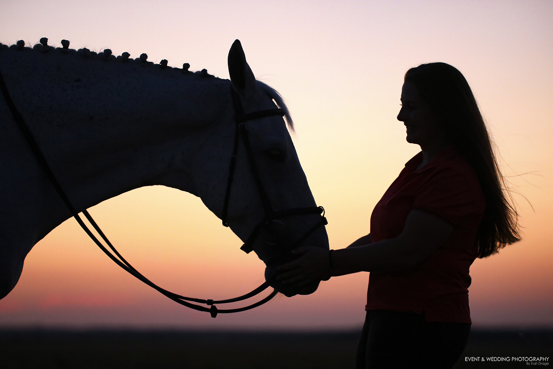 Silhouetted shot of female rider stroking her horse's nose at sunset