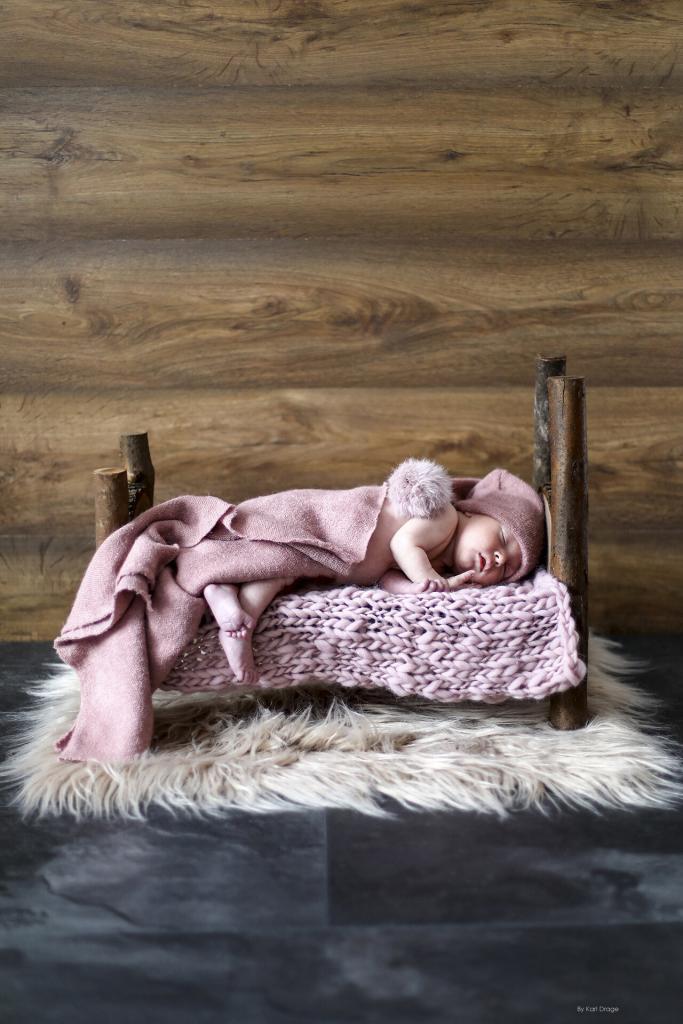 Newborn baby girl asleep on a natural wooden bed photo prop