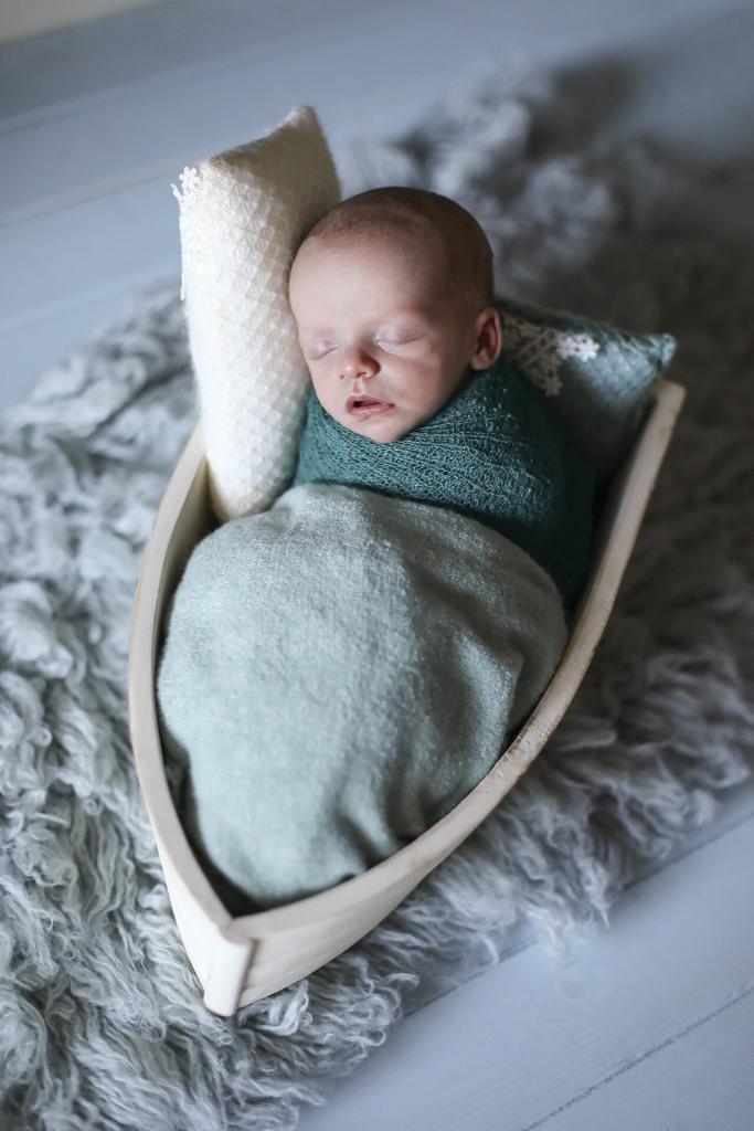 A newborn baby boy asleep on the ocean in his wooden boat photo prop