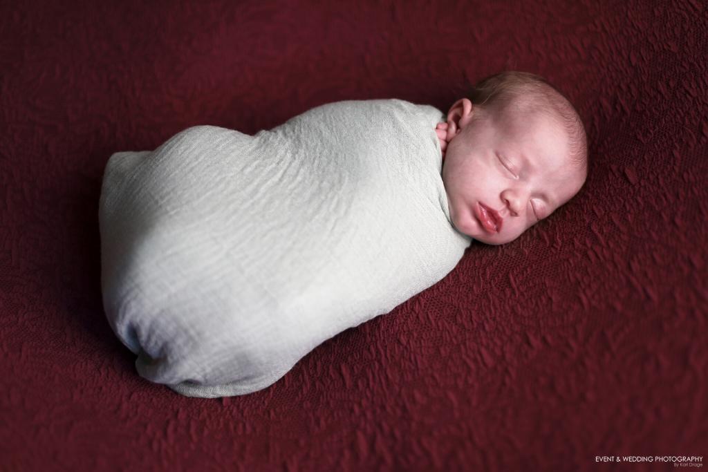 Newborn baby girl asleep on a burgundy Oslo fabric blanket