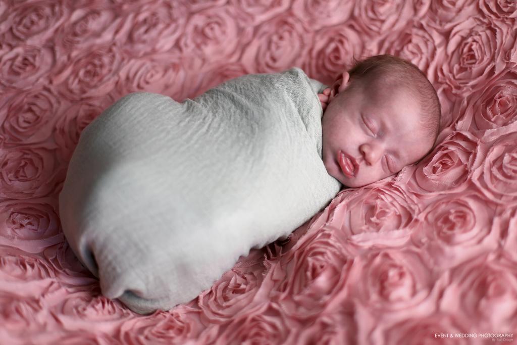 Wrapped baby girl asleep on a dusty pink flower fabric blanket