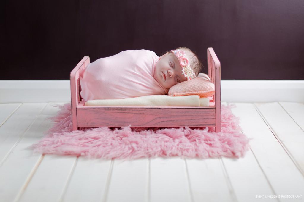 Newborn baby girl asleep on a pink wooden bed