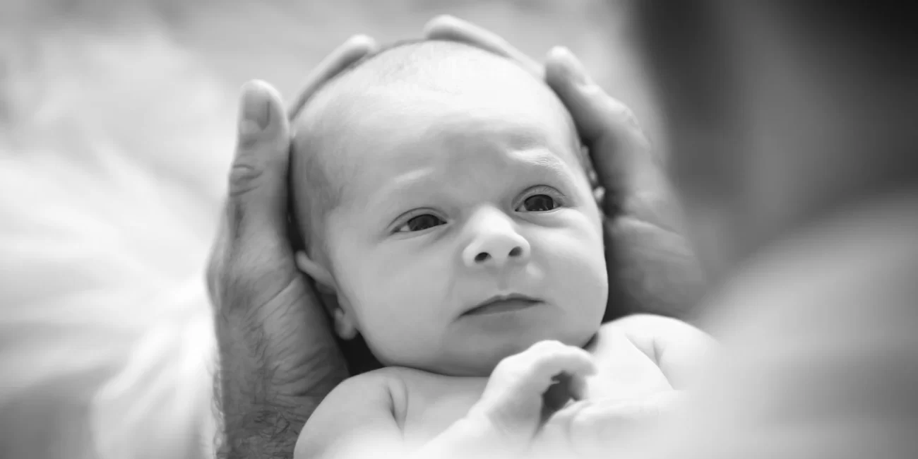 A baby girl's head is cradled by her dad's hands as she stares back at him adoringly