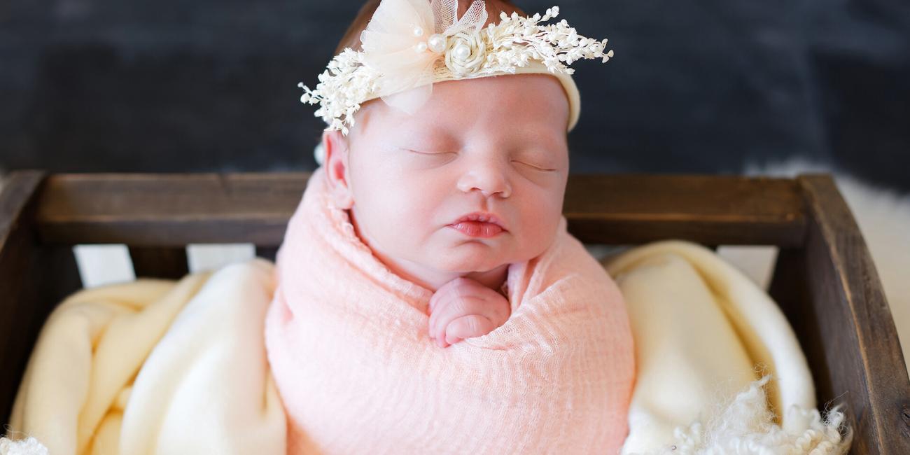 Wrapped newborn baby asleep in a wooden crib during her first photo shoot