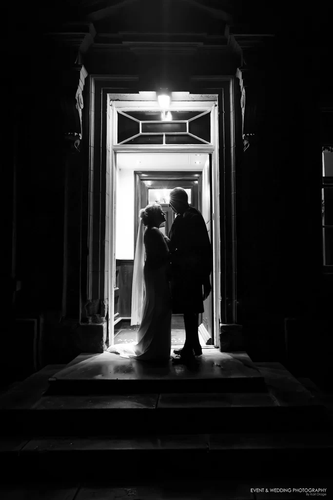 A black and white silhouette of a bride and groom stood in the doorway to Ansty Hall on their wedding day