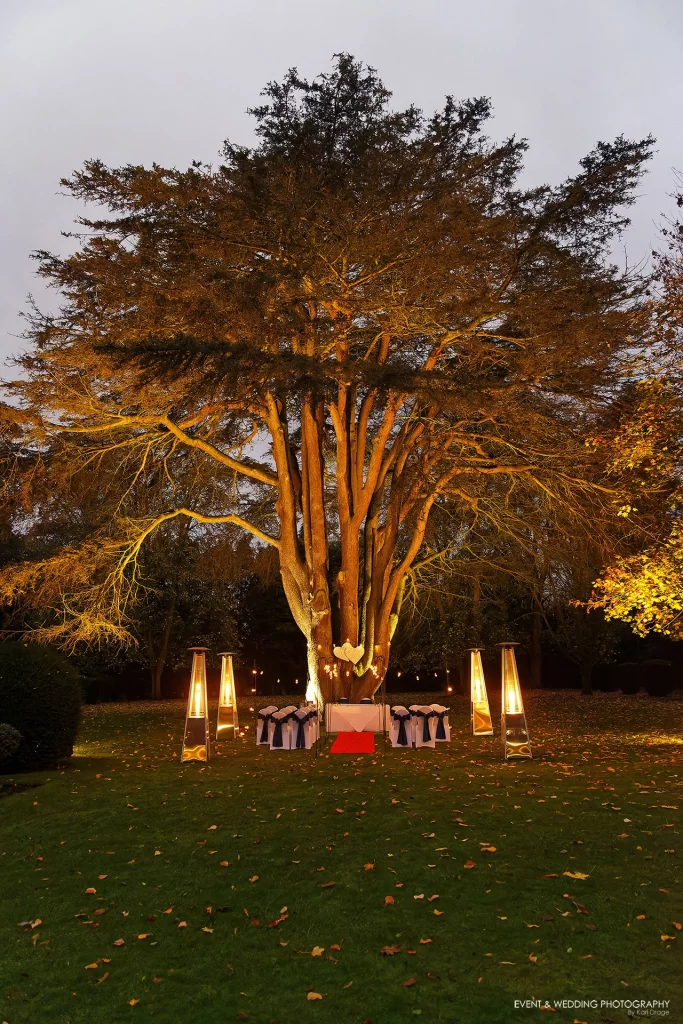 The setup for an after-dark outdoor wedding ceremony in front of the big tree at Ansty Hall