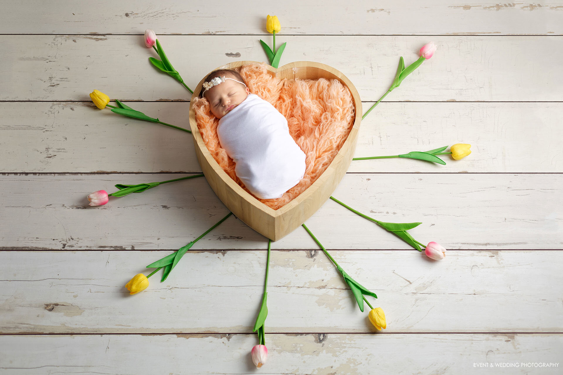A newborn baby girl asleep in a heart-shaped wooden photo prop
