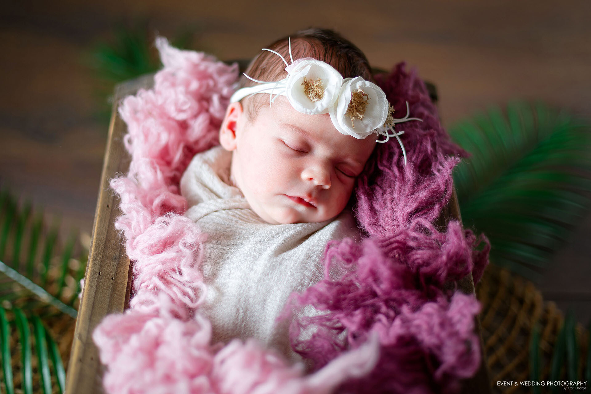 Newborn baby girl wearing a floral headband asleep in a wooden crib photo prop