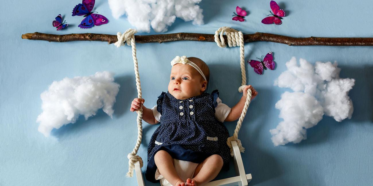 Baby Piper swings among the clouds and butterflies during her newborn photo shoot