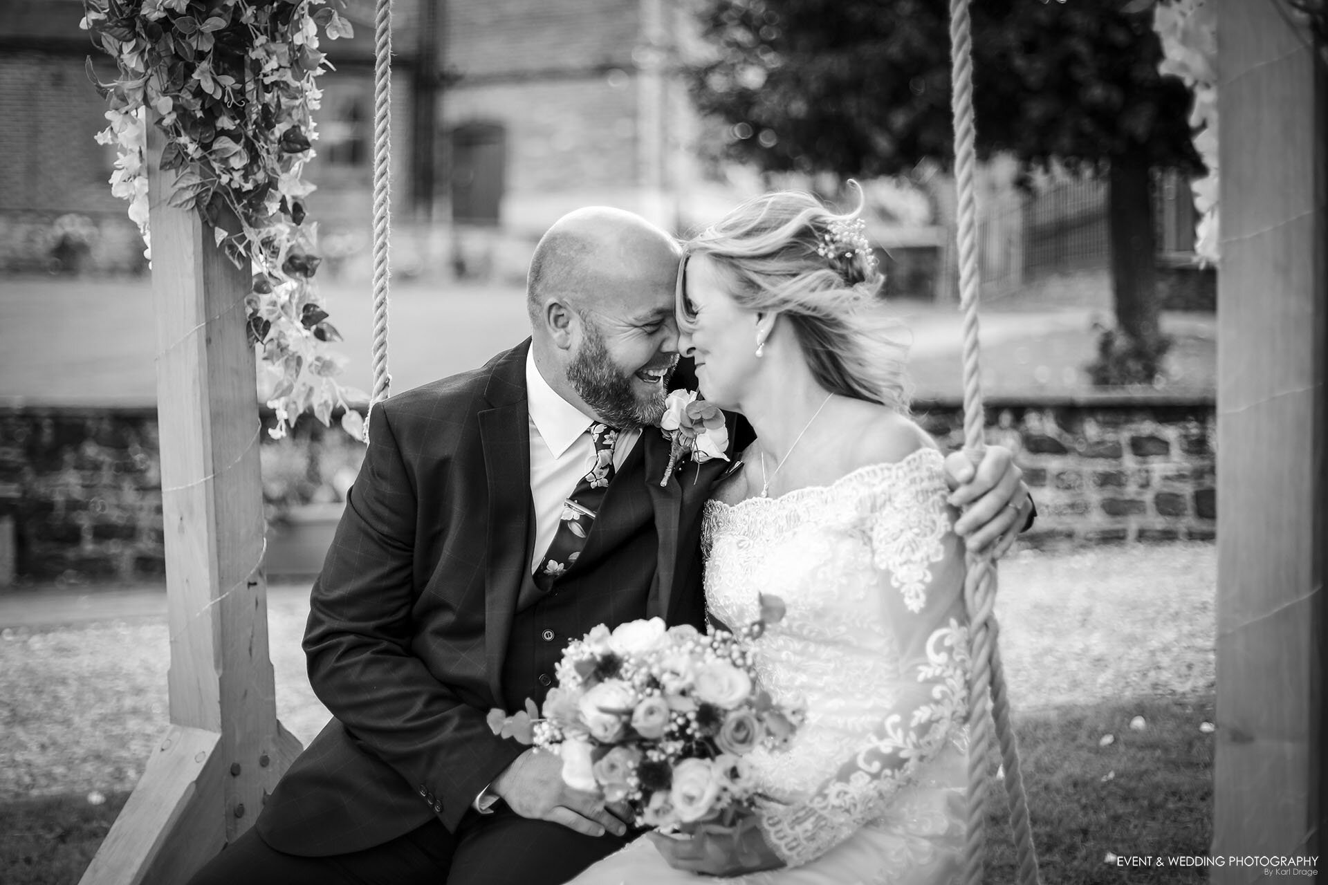 Black and white shot of a bride and groom putting their heads together while sat on a special wedding swing at their The Barns at Hunsbury Hill wedding