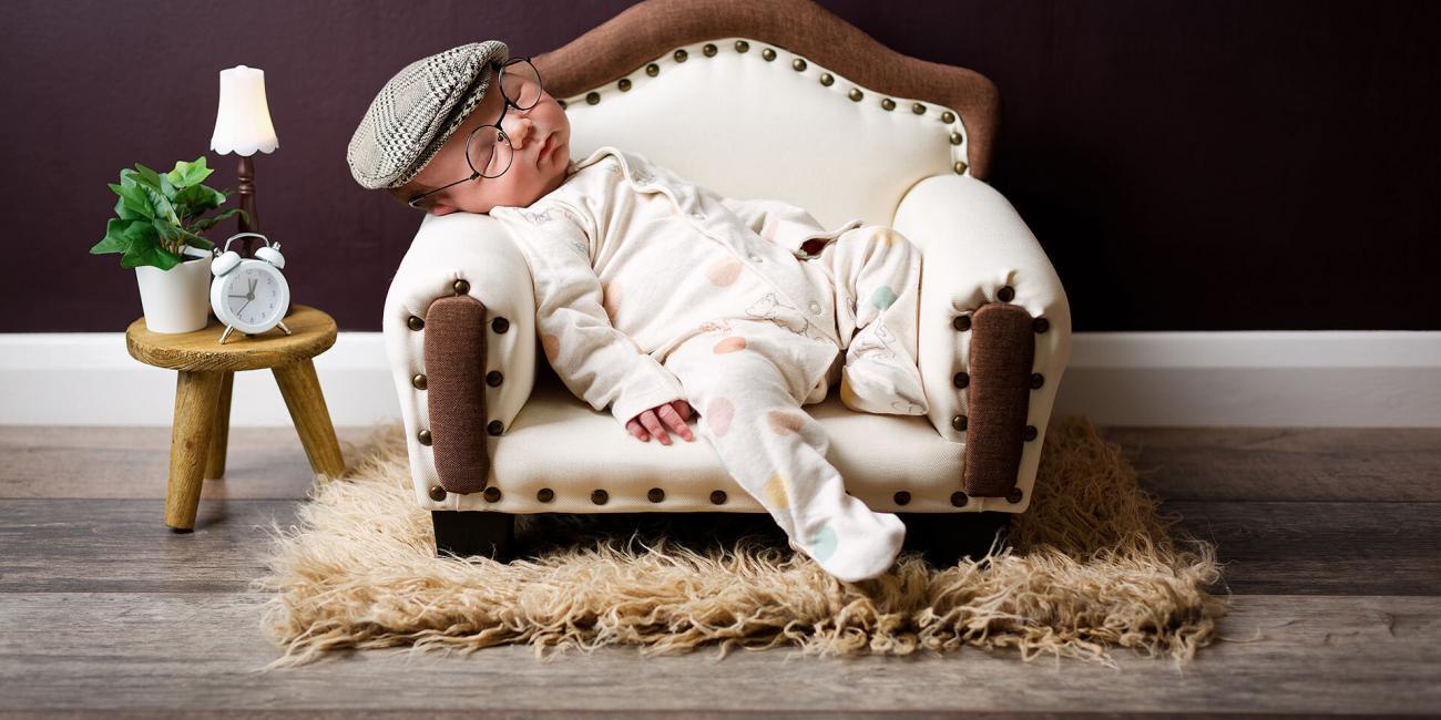 Newborn baby boy asleep in a white upholstered sofa during his newborn photo shoot in a Northampton newborn photo studio