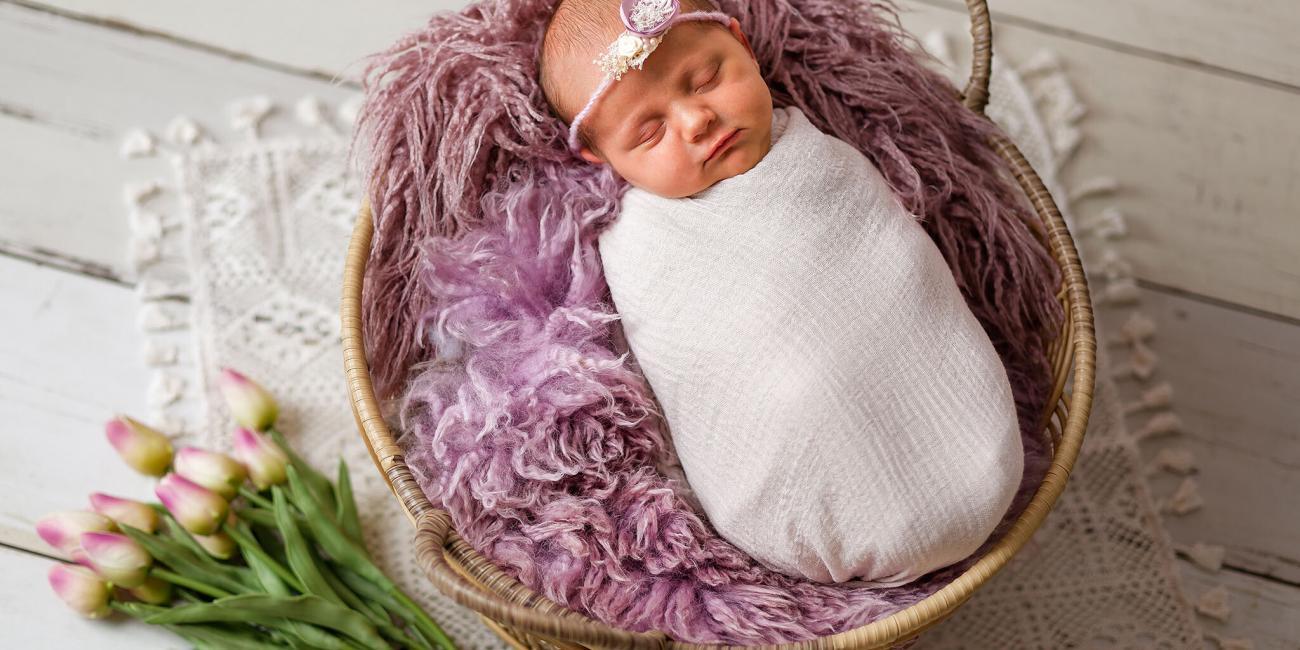 A baby girl sleeps in a rattan basket during her Wellingborough newborn photo shoot.