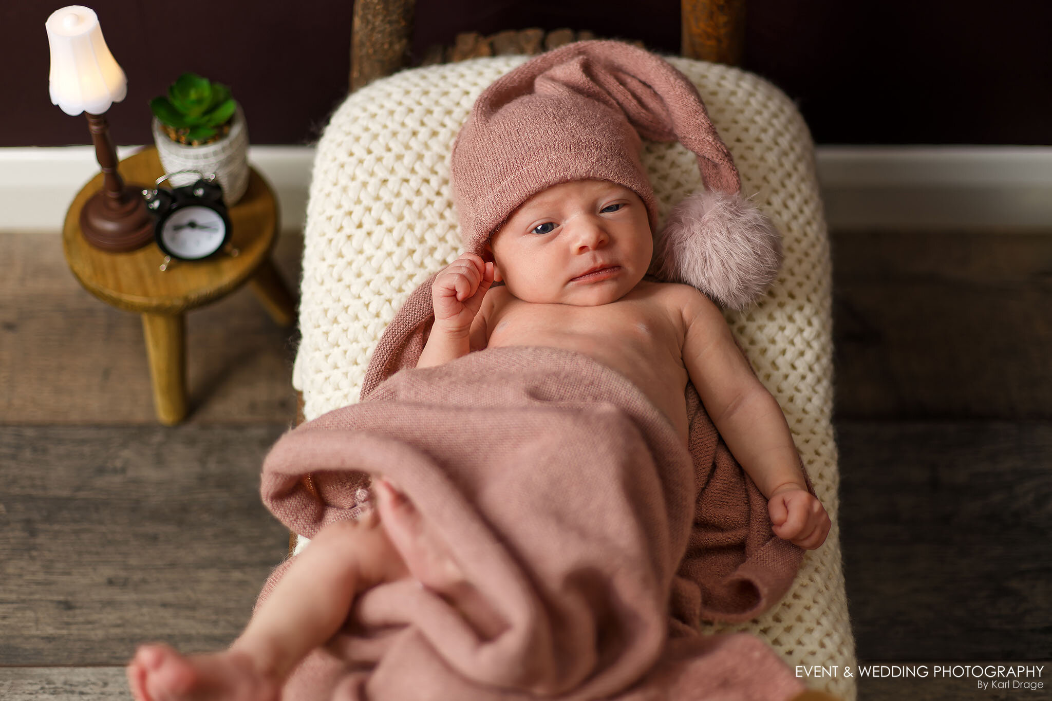 A newborn baby girl lays wide awake in a rustic wooden bed during her photo shoot with Kettering newborn photographer Karl Drage