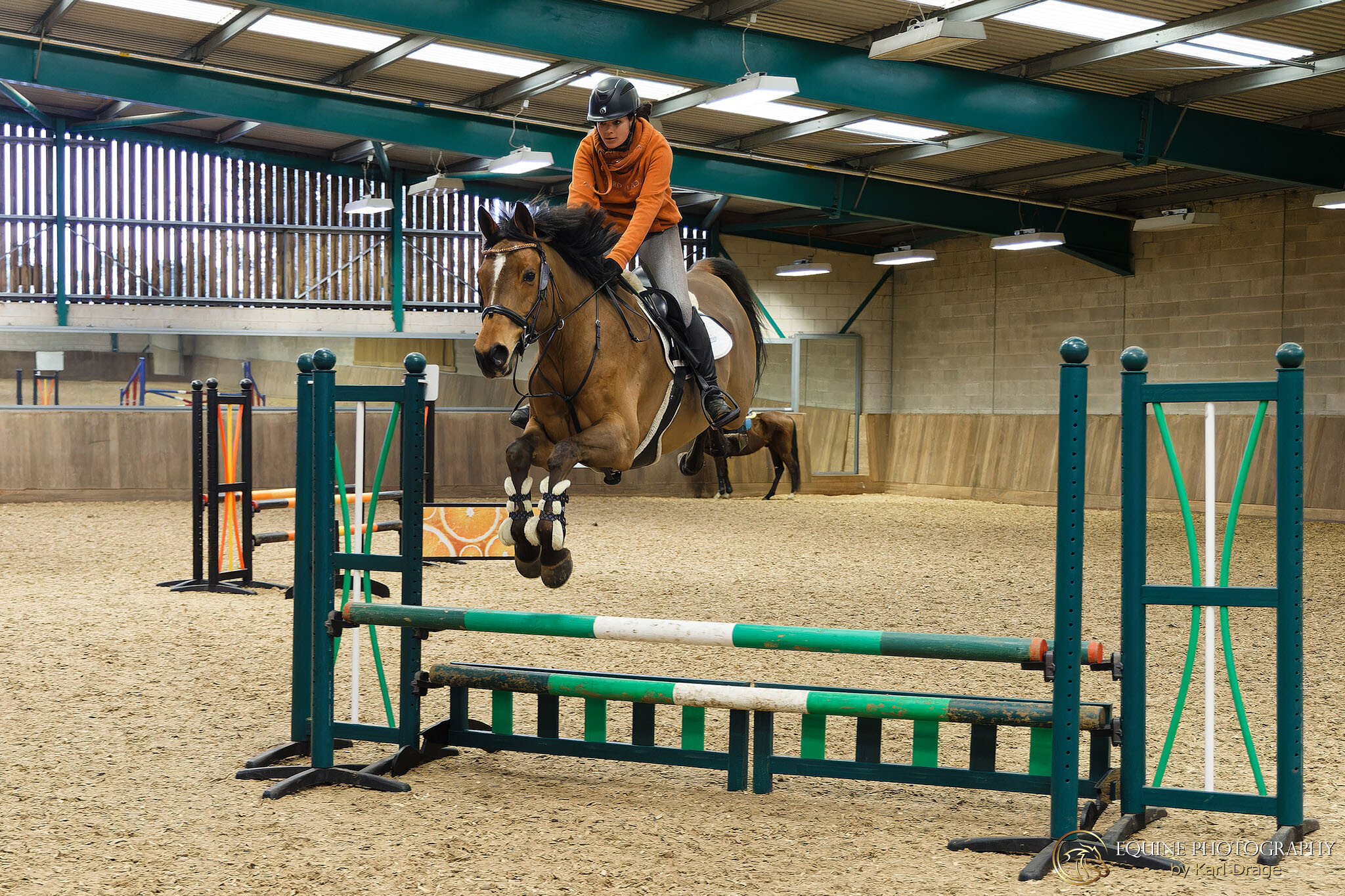 A gelding soars over a pole during an indoor arena hire session at Moulton College Equestrian Centre.