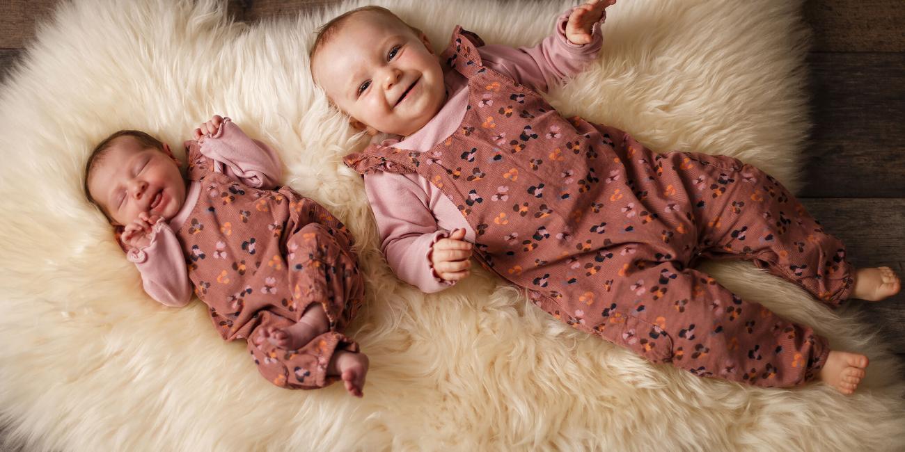 A newborn baby girl and her big sister lay on a sheepskin rug during the newborn's first photo shoot.