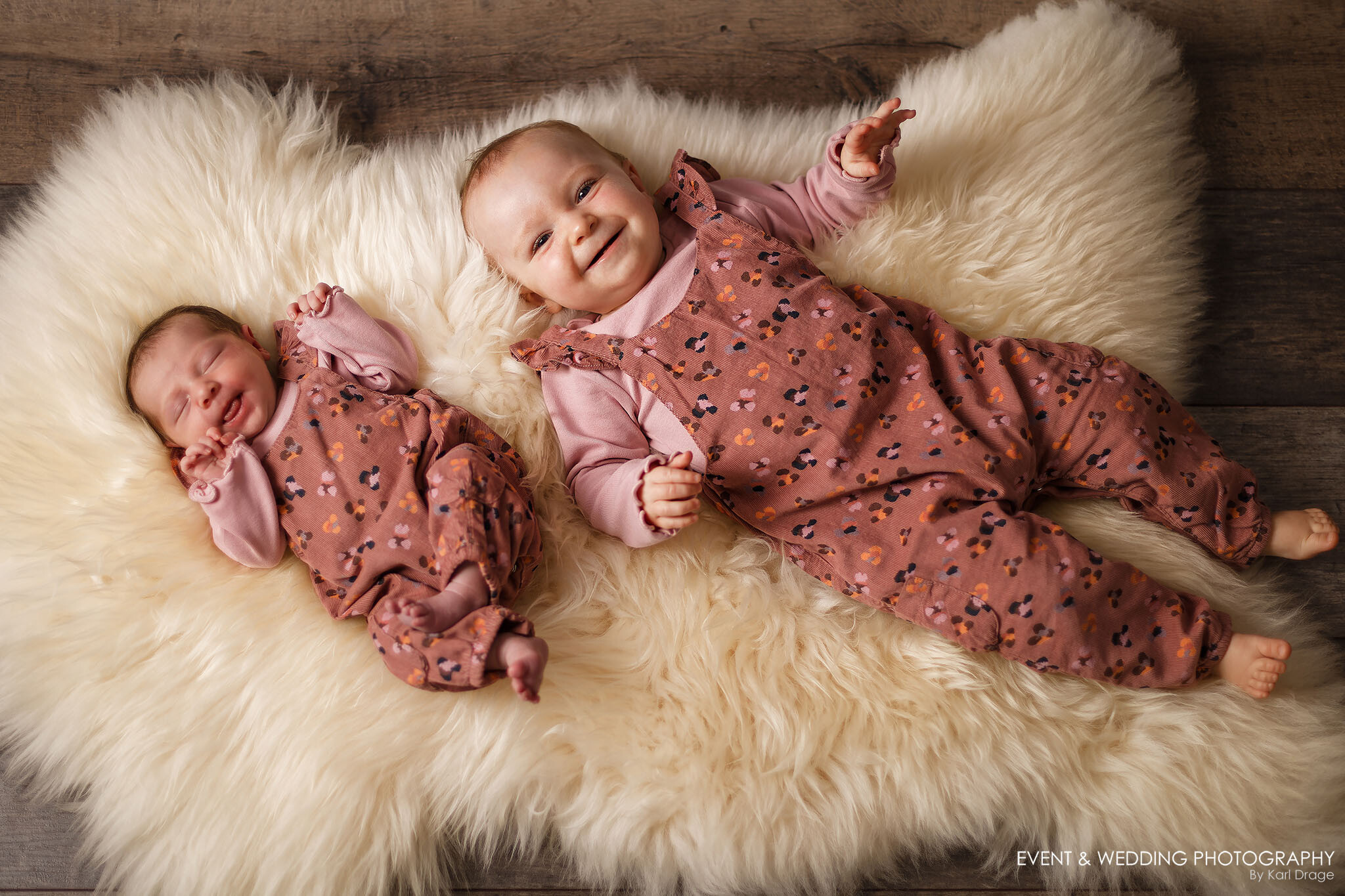 A newborn baby girl and her big sister lay on a sheepskin rug during the newborn's first photo shoot.