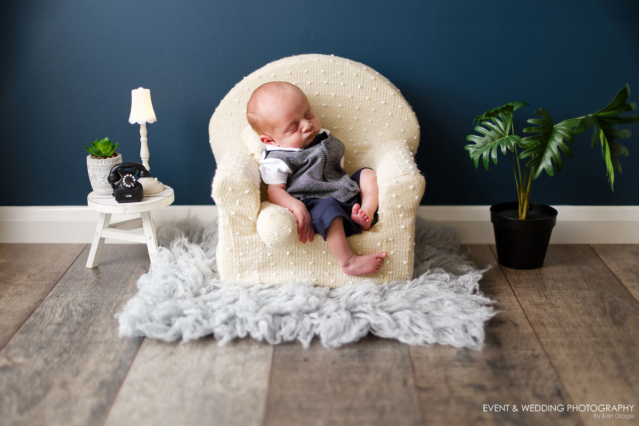 A baby boy fast asleep in a white woollen armchair.