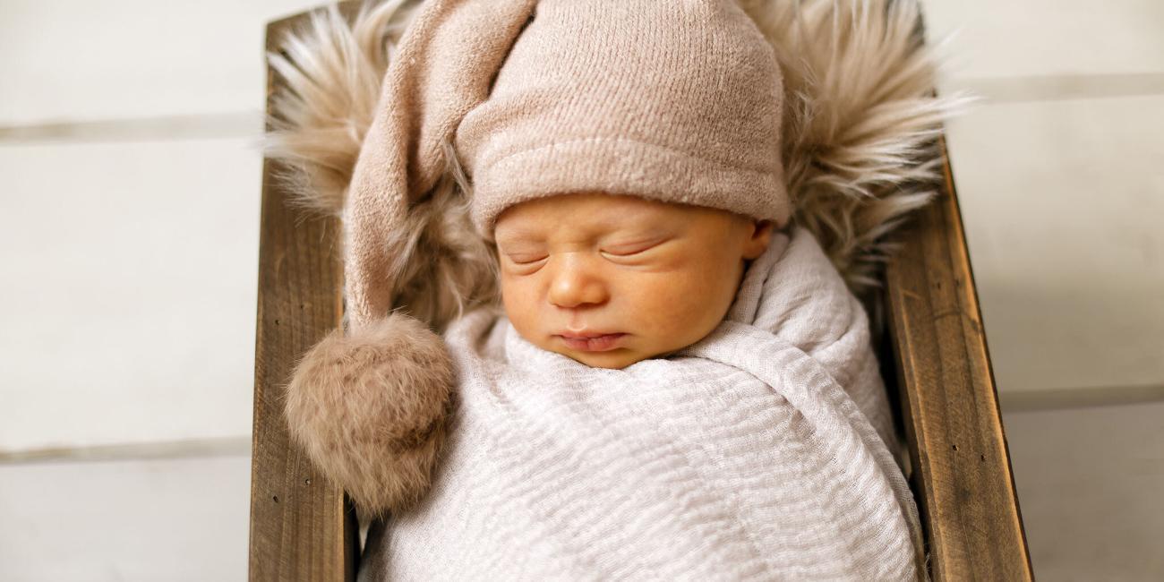 A wrapped newborn baby boy asleep in a rustic wooden crib pictured during his Northampton baby photo shoot.